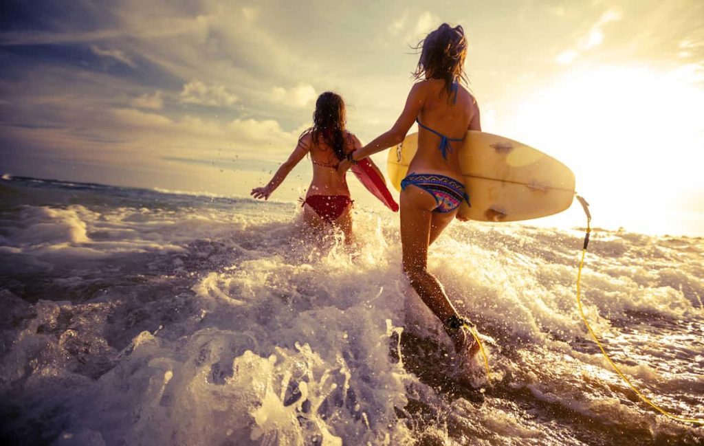 Surfers carrying boards into the ocean at sunset in Kuta Lombok, Indonesia.
