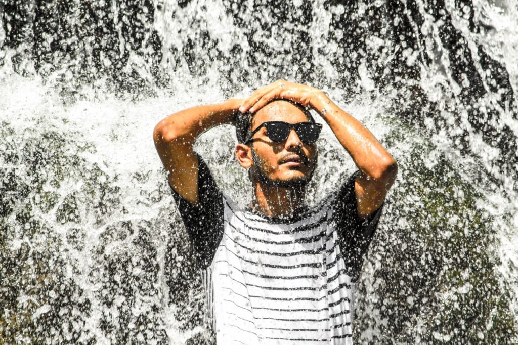 man wears shades under a waterfall in Luang Prabang