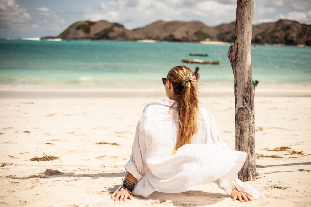 Girl sitting on the beach looking out at the waves